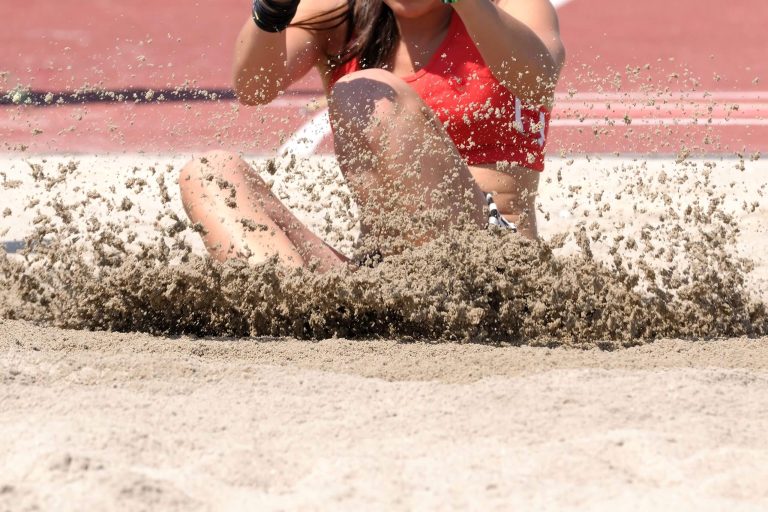 Athletin beim Weitsprung mit aufgewirbeltem Sand – typischer Einsatzbereich für gewaschenen Quarzsand der Quarzwerke Friedl auf Leichtathletikanlagen